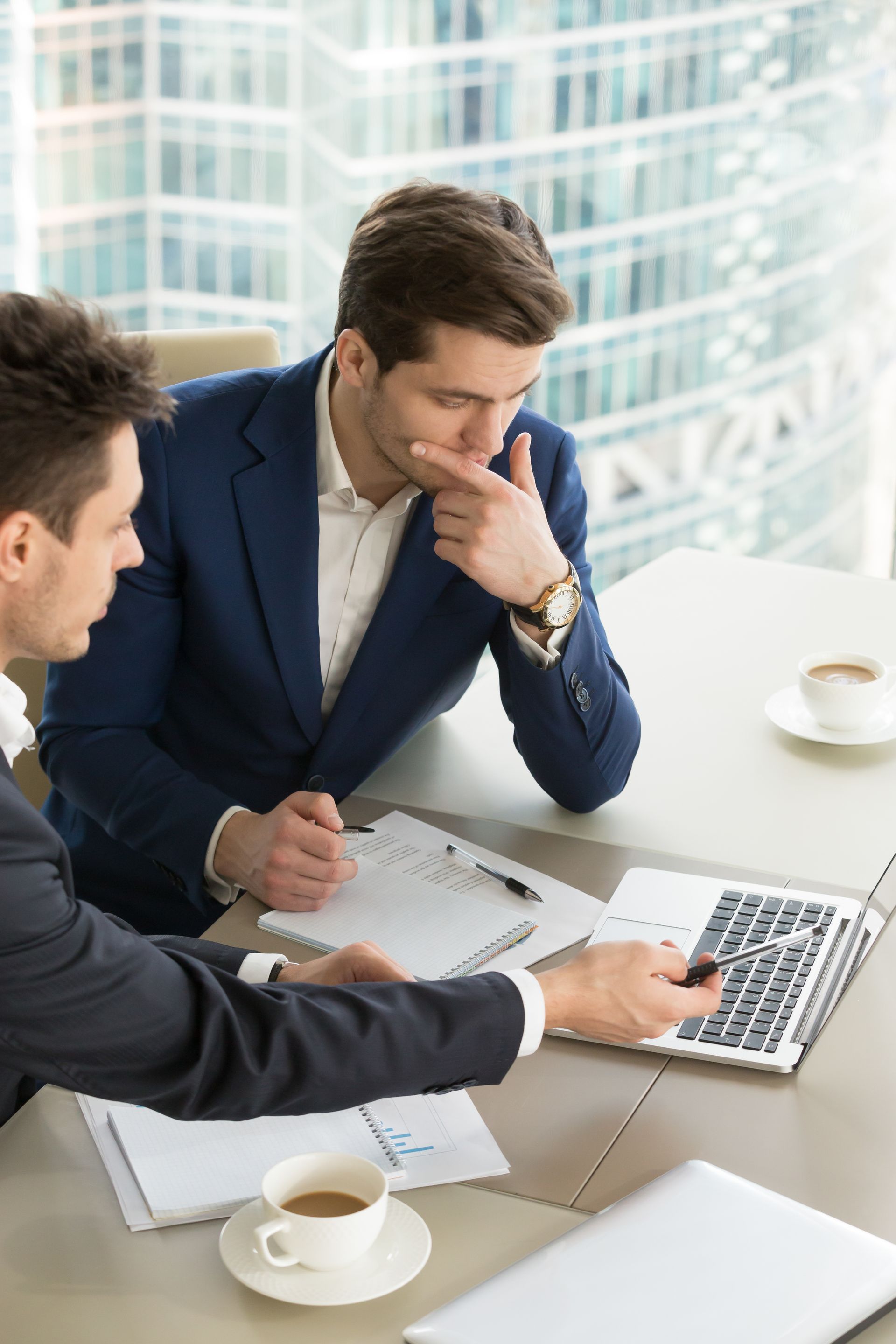 Dos hombres están sentados en una mesa mirando una computadora portátil.