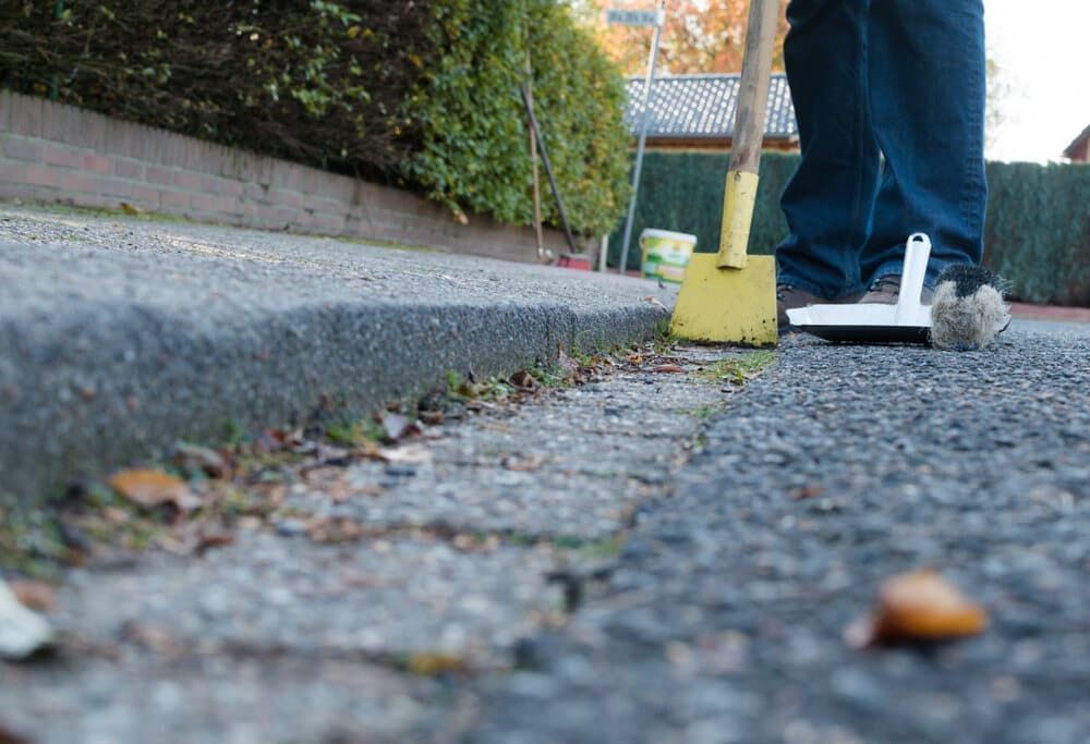 Person Sweeping a Sidewalk Gutter With a Yellow Broom — Cleanaroo Property Services in Conder, ACT