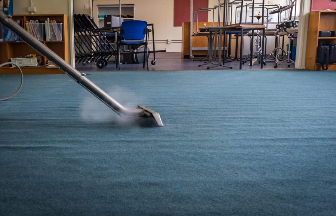 Steam Cleaner Moving Across a Blue Carpet in a Room With Shelves and Furniture — Cleanaroo Property Services in Conder, ACT
