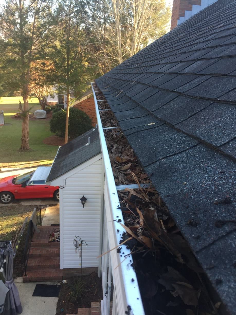 A gutter with leaves on it is on the side of a house.