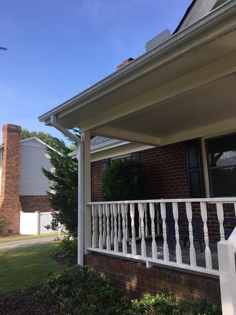 A porch with a white railing and a chimney in the background