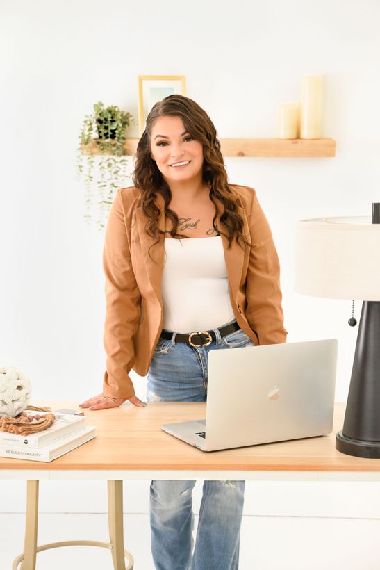 A woman is sitting at a desk with a laptop and a vase of flowers.