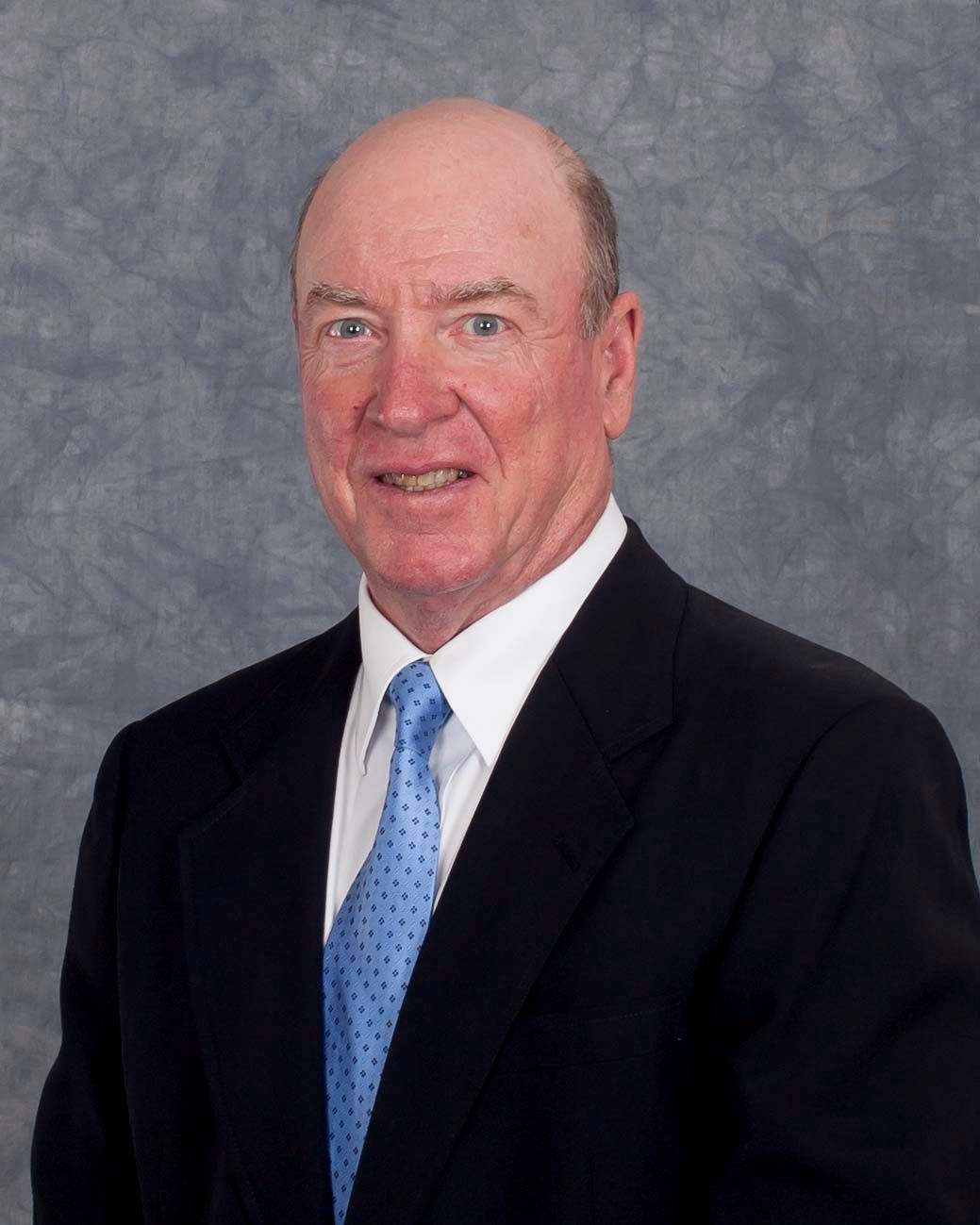 Man in a suit smiles, blue tie, on a textured blue-gray background.