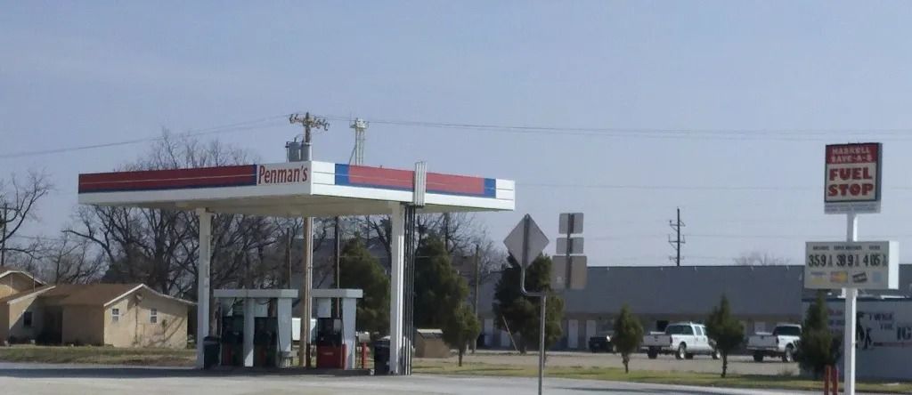 Gas station with a red and blue canopy. Fuel Stop sign nearby, two cars parked in the background.