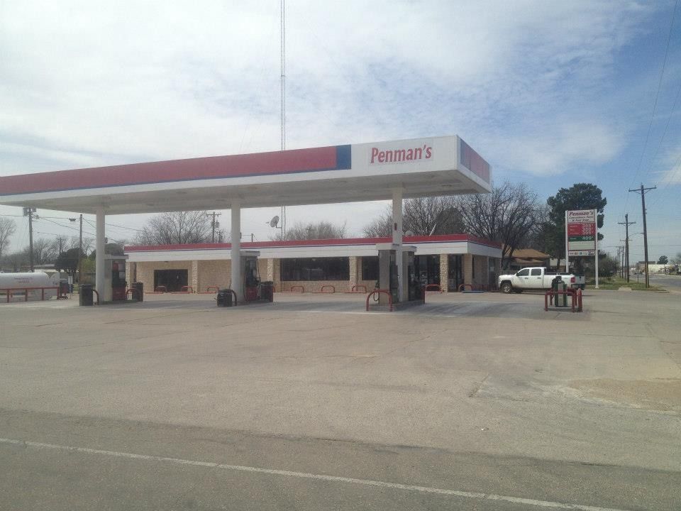 A gas station with a red and white canopy, a store, and a white pickup truck on a sunny day.