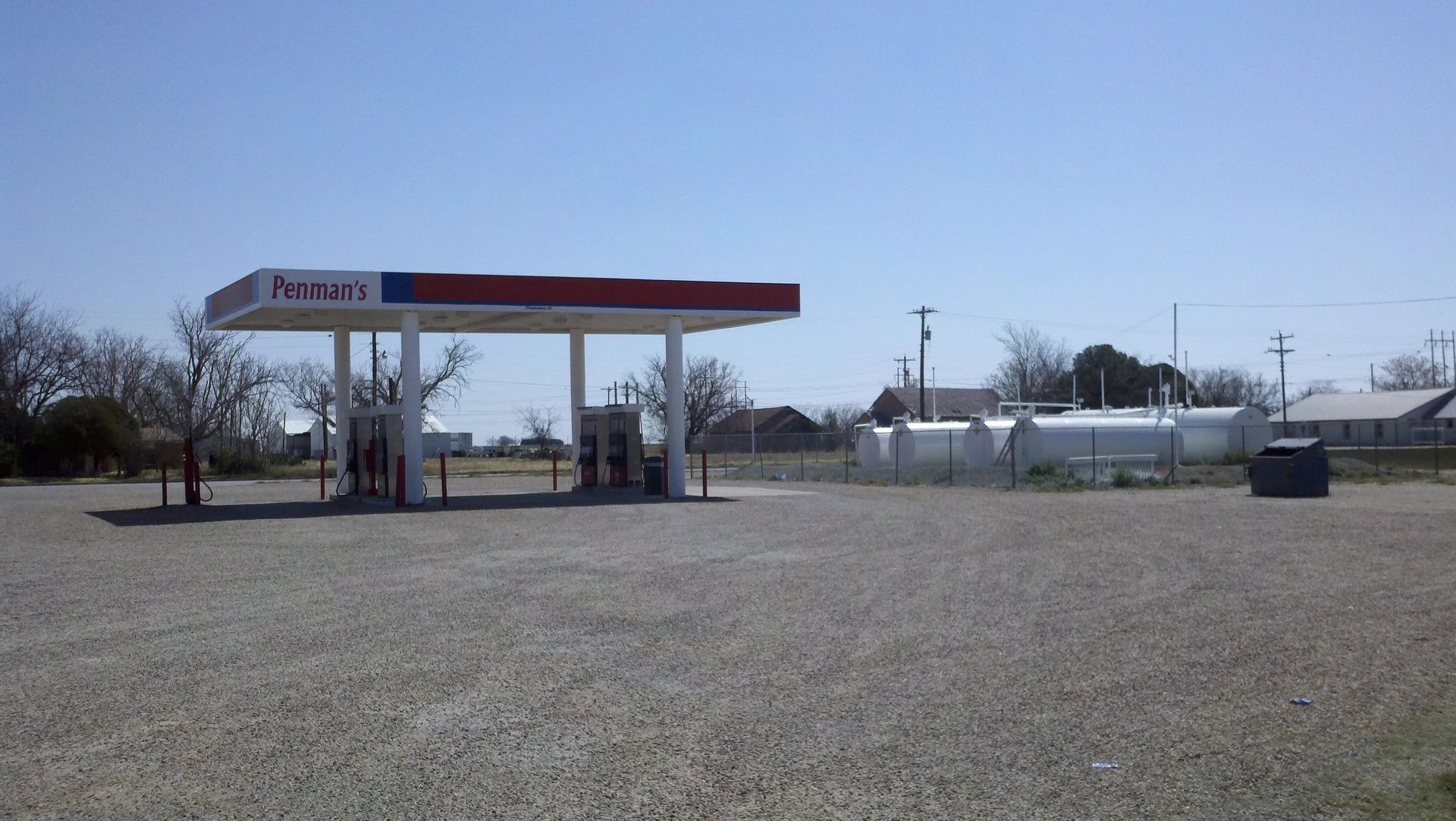 Gas station with red and blue canopy; gravel lot; white fuel tanks in the background.