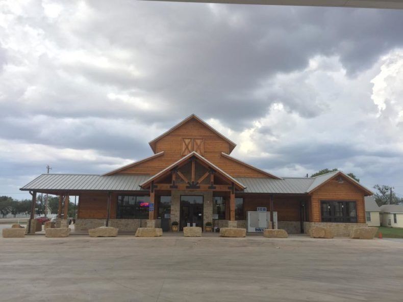 Wooden building with stone accents, a covered entrance, and a cloudy sky backdrop.