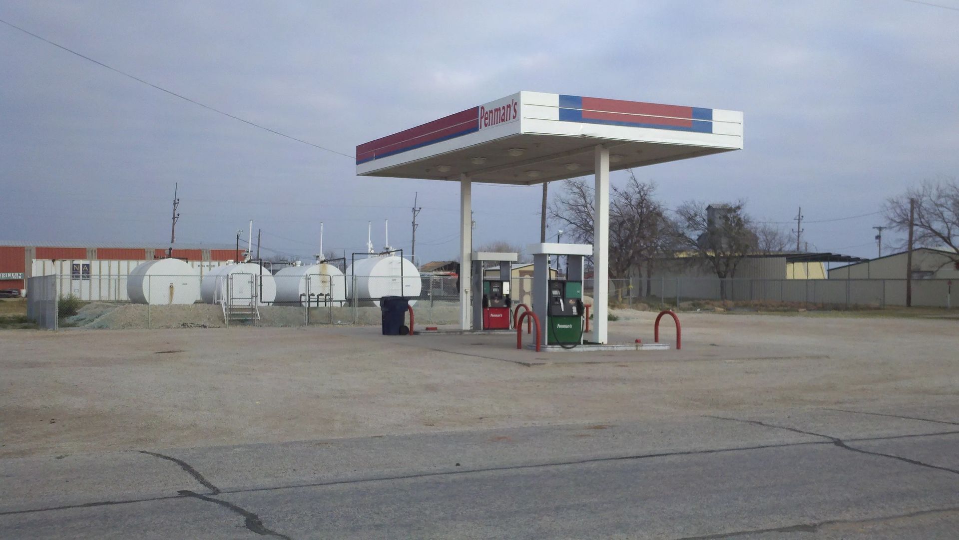 Gas station with a white canopy, gas pumps, and tanks, under a cloudy sky.