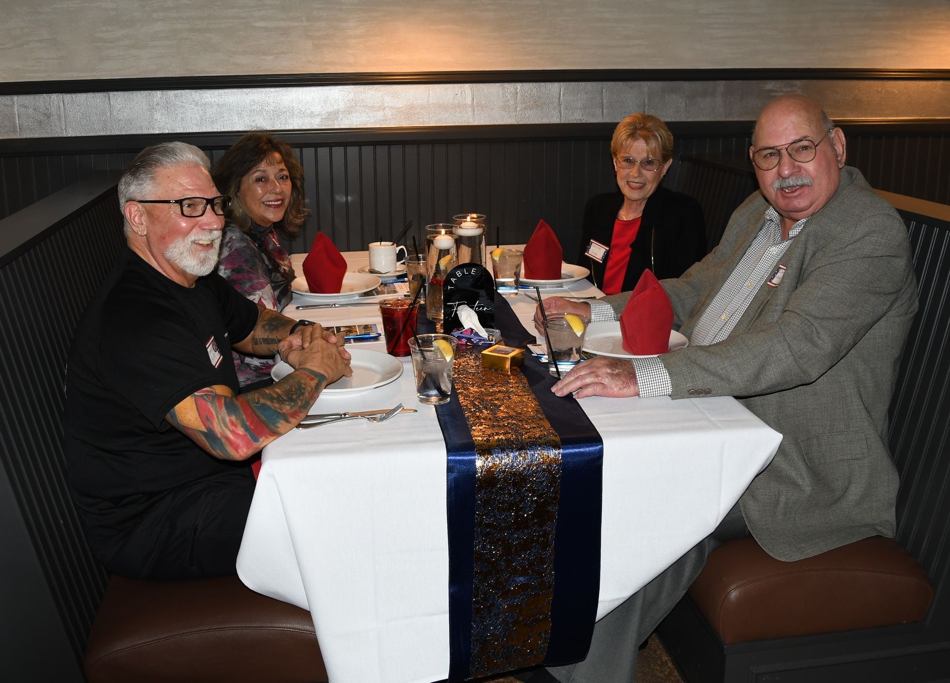 Four people seated at a restaurant table with drinks and a centerpiece, smiling toward the camera.