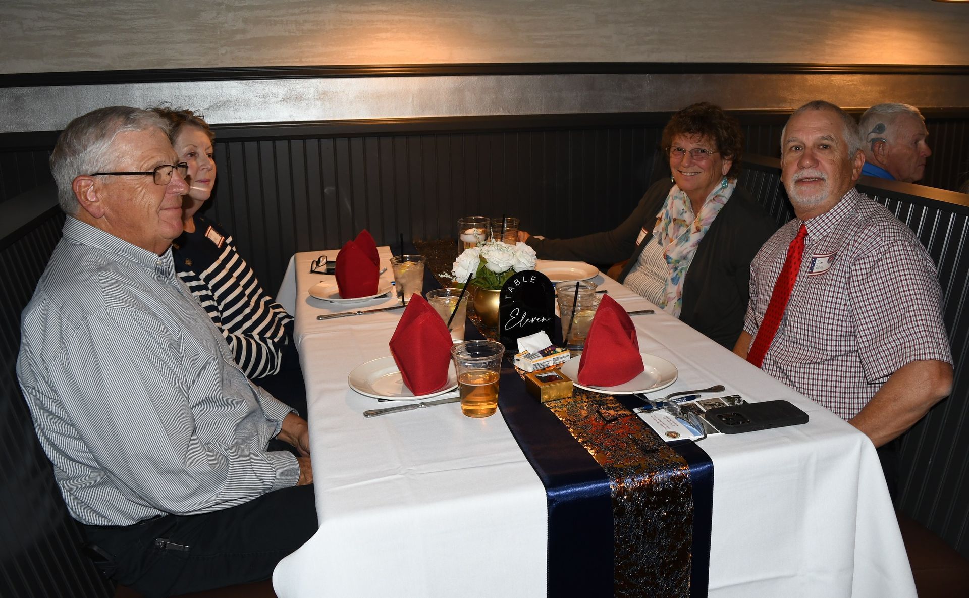 People seated at a restaurant table with folded red napkins and a white tablecloth, smiling at the camera