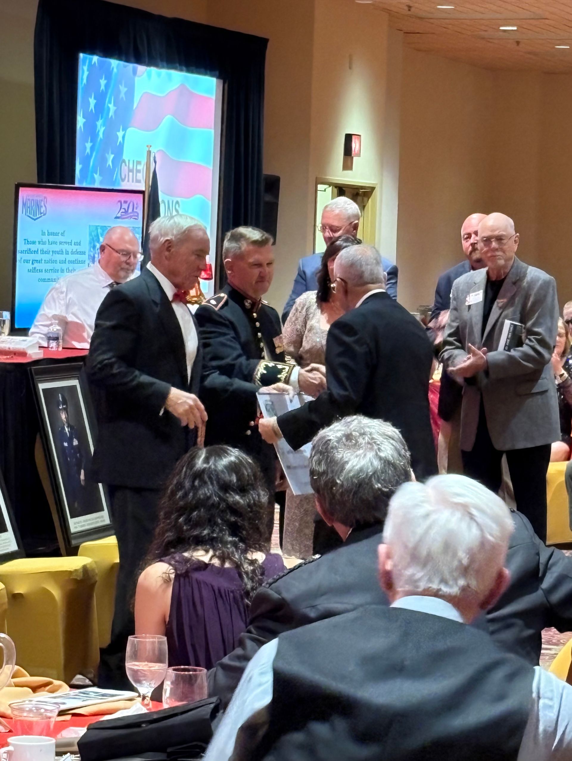 People mingling at a formal indoor event with a presentation screen and display boards in the background