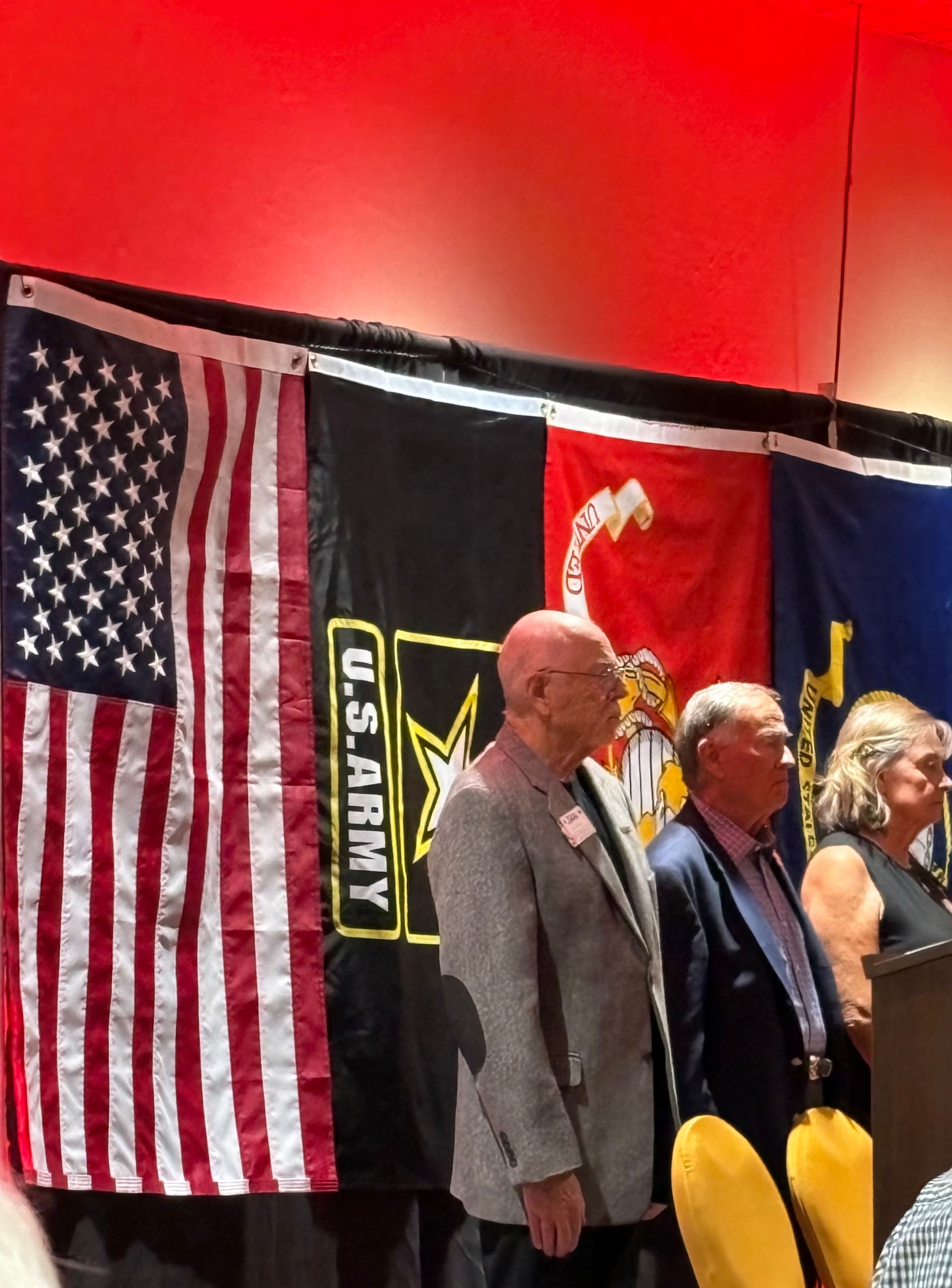 Three people standing before U.S. military flags at a formal indoor event