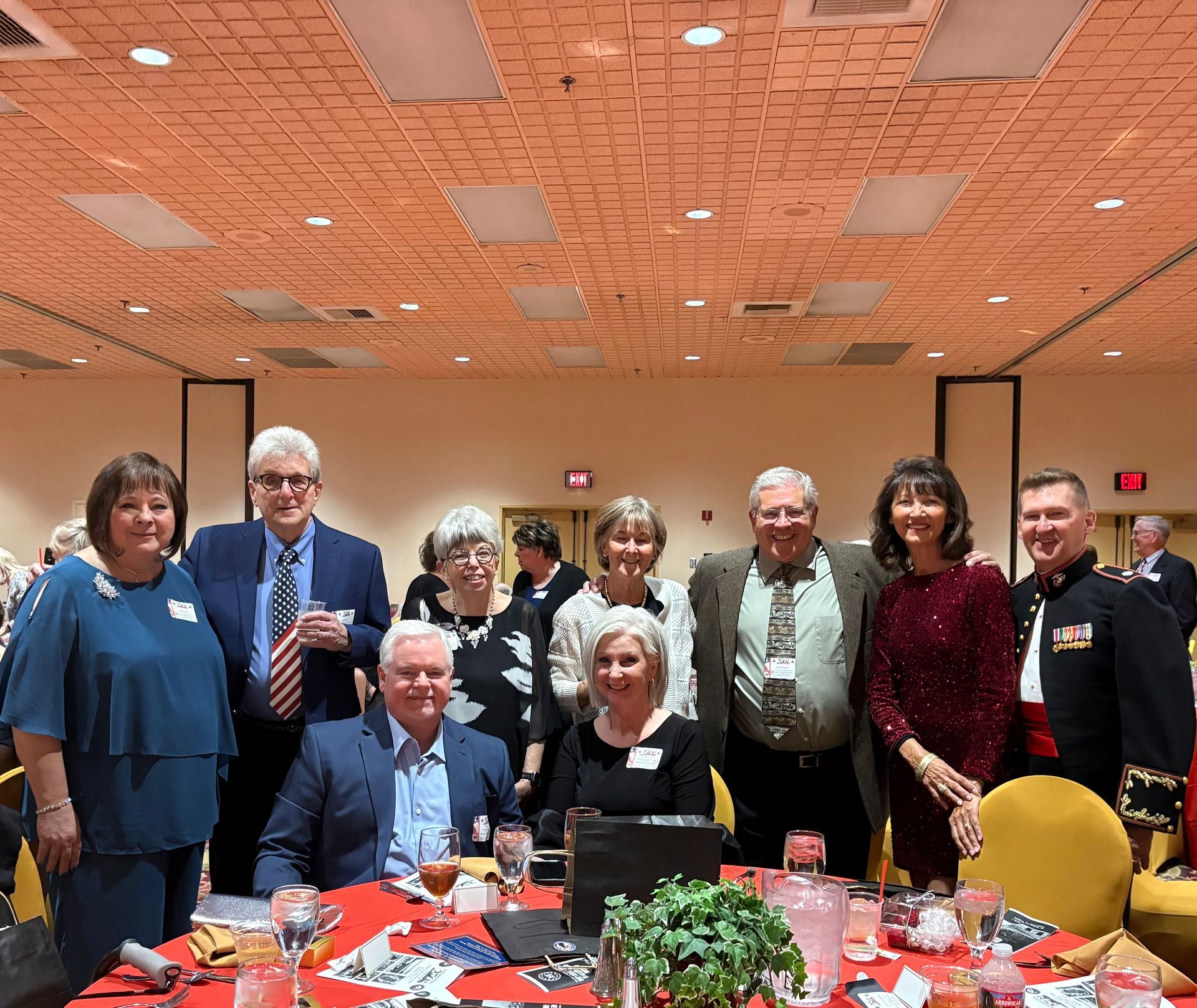 Group of people posing around a decorated banquet table at an indoor event with orange ceiling lights.