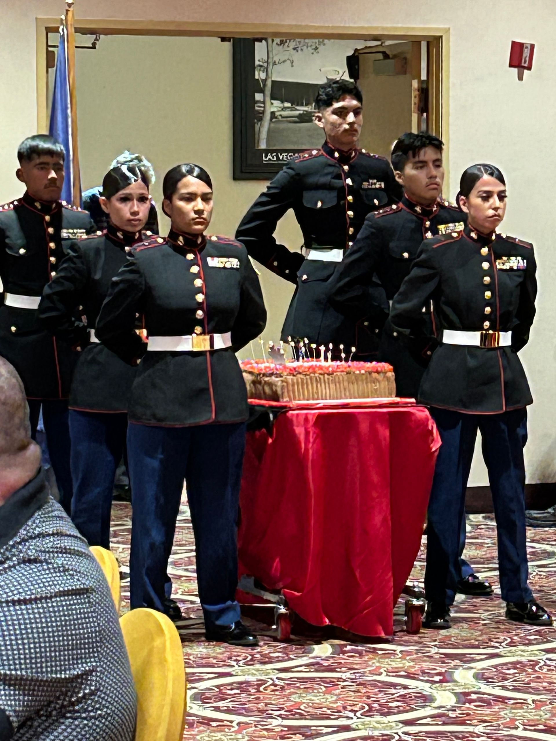 Uniformed cadets standing at attention beside a red-draped table in a hall