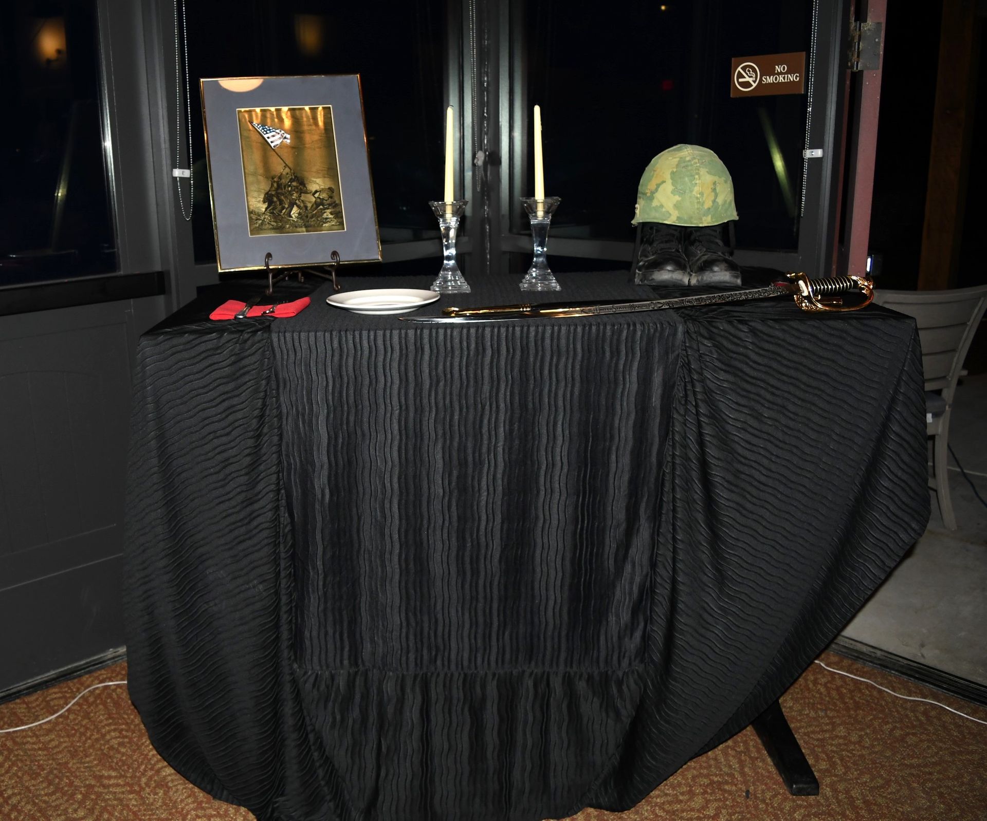 Black-draped display table with silver candlesticks, framed item, red glasses, and a green decorative object on top