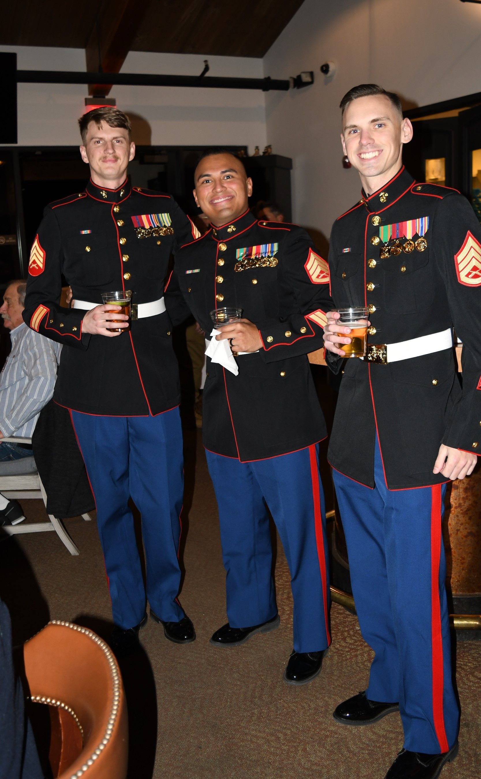 Three Marines in dress blues holding drinks at an indoor event
