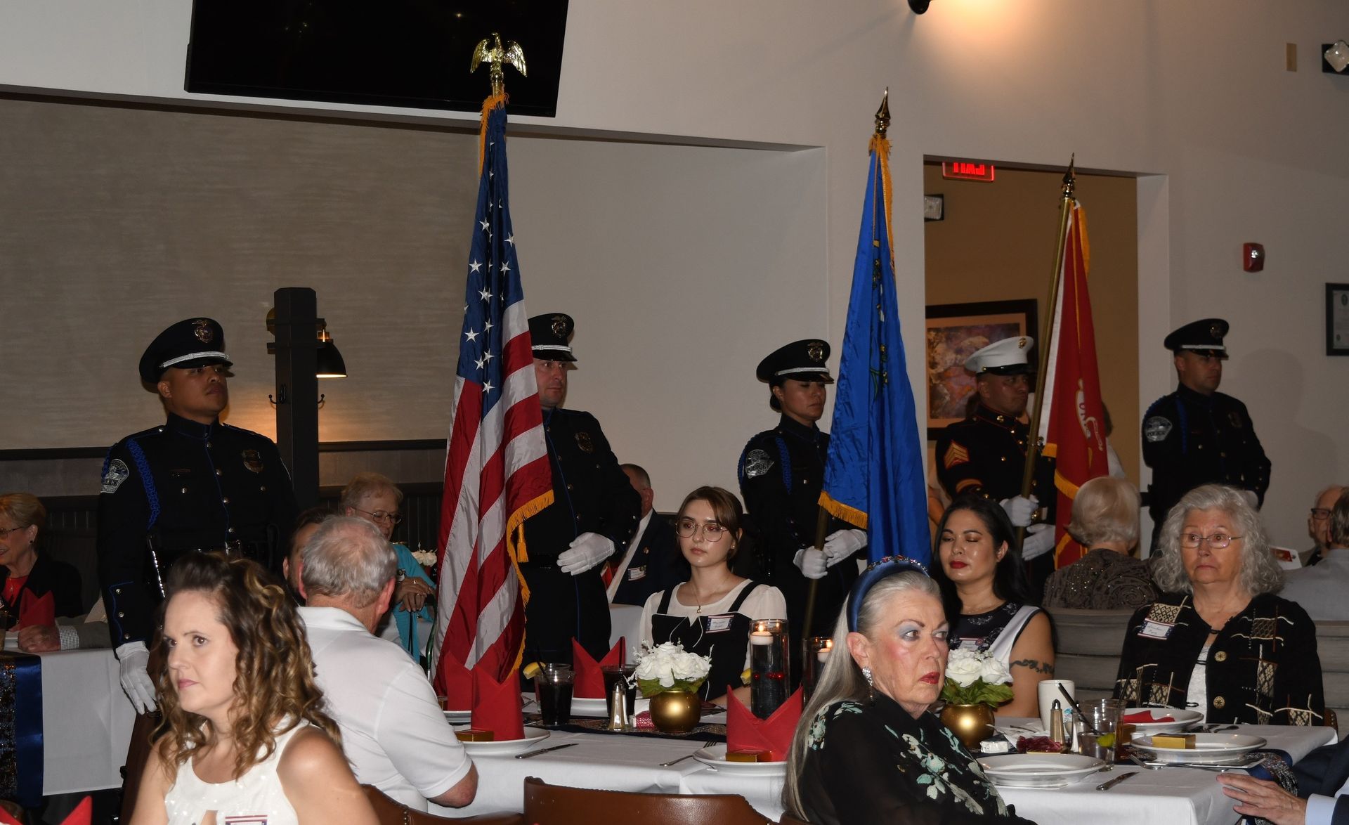 People seated at a banquet table with police officers and flags in the background