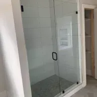 Glass shower enclosure with white tile and a tiled shower floor.