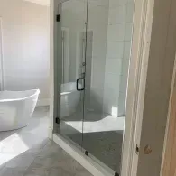 Modern bathroom with glass shower enclosure and white bathtub, lit by sunlight