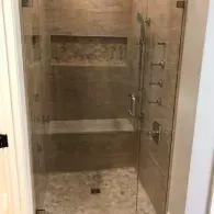 Tiled walk-in shower with glass door, built-in bench, and wall shelves
