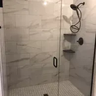 Glass shower with white tile walls, mosaic floor, black fixtures, and corner shelves.