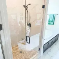 Glass shower enclosure in a bright bathroom with pebble floor and vanity sink nearby