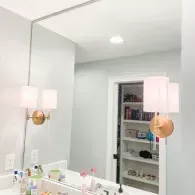 Bright bathroom vanity with large mirror, wall sconces, sink, and open shelving in the reflection