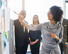 A woman is pointing at a whiteboard in front of a group of people.