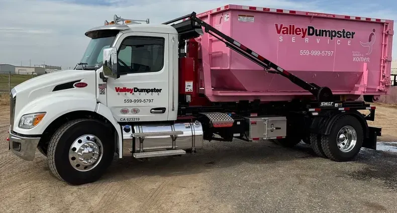 White dump truck with pink Valley Dumpster container parked on gravel lot