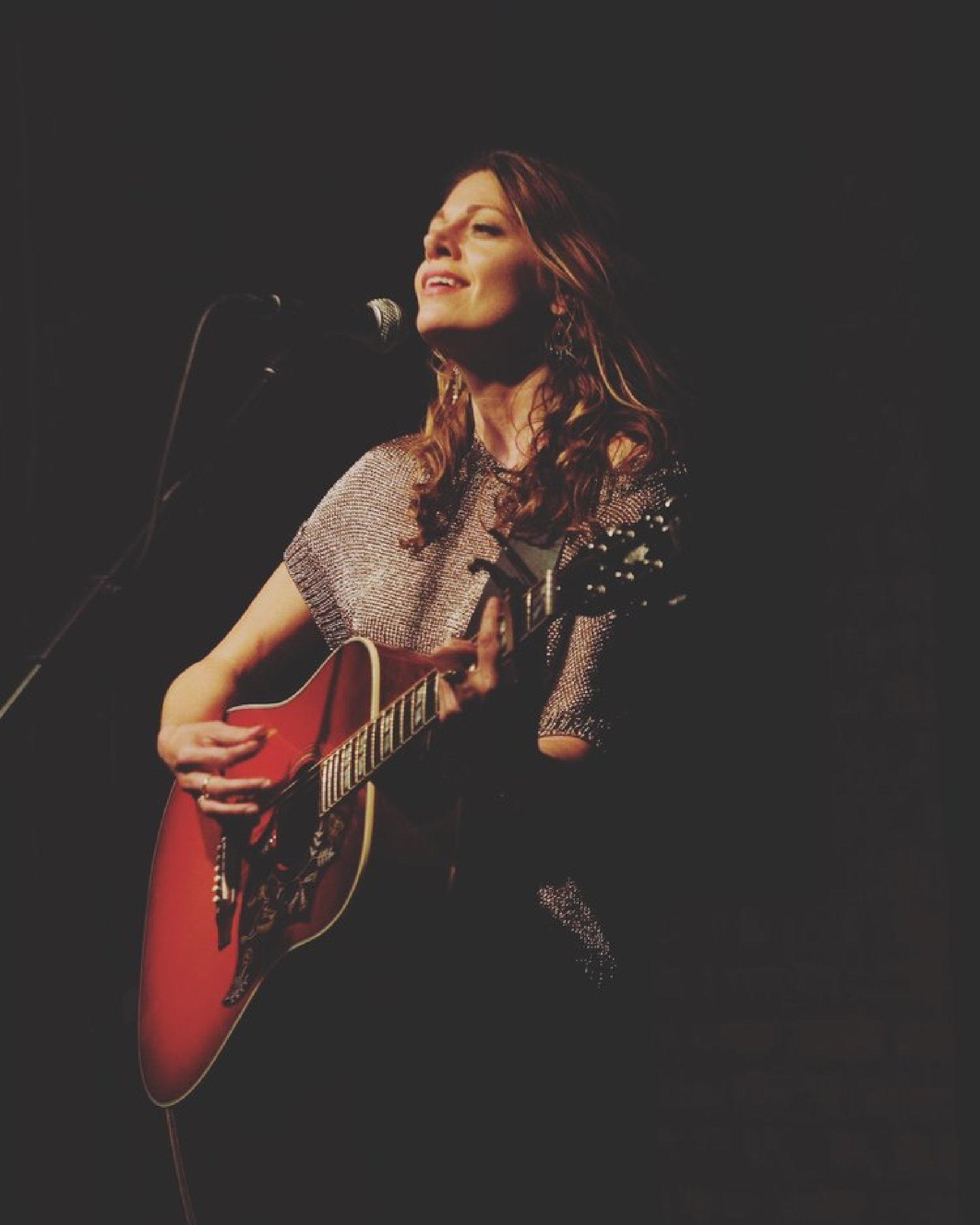 A woman singing into a microphone while holding a guitar