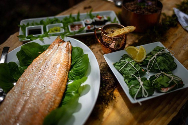A wooden table topped with plates of food , including a piece of salmon.