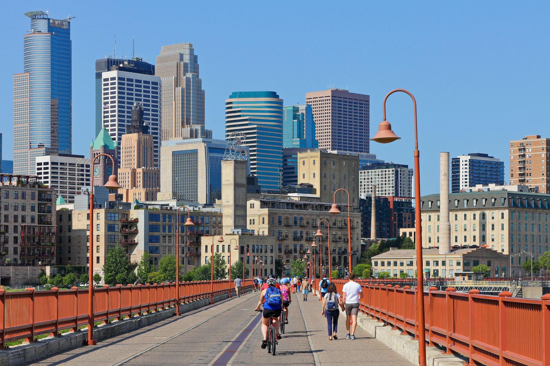 A group of people are walking across a bridge in front of a city skyline.