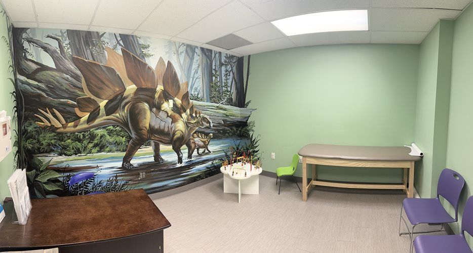 Office with a large dinosaur mural, green walls, desk, small table, and chairs.