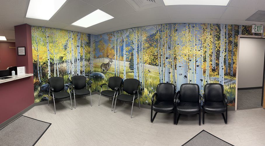 Waiting area with black chairs, birch tree mural, and reception desk in a clinic or office lobby.
