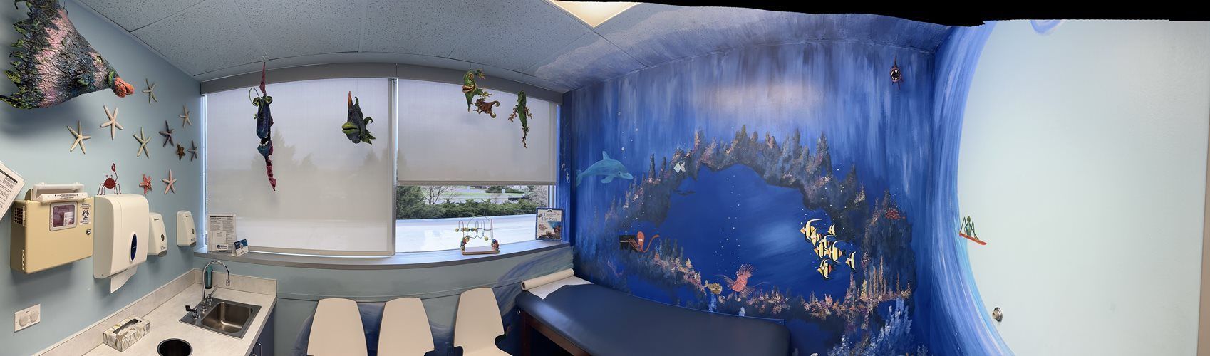 Curved blue-walled room with whale mural, aquarium decor, and rows of chairs beside a desk area