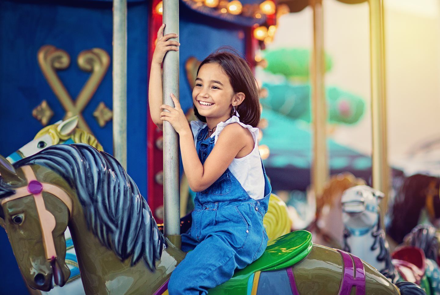 Child smiling on a carousel horse, holding the pole on a colorful merry-go-round