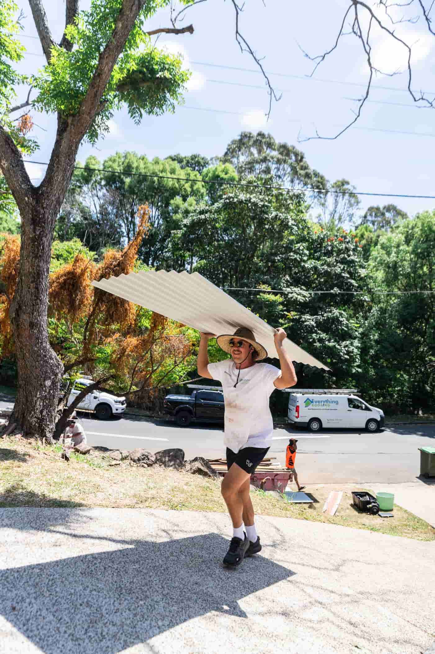 Man on a roof using a nail gun; installing roofing material on a sunny day.