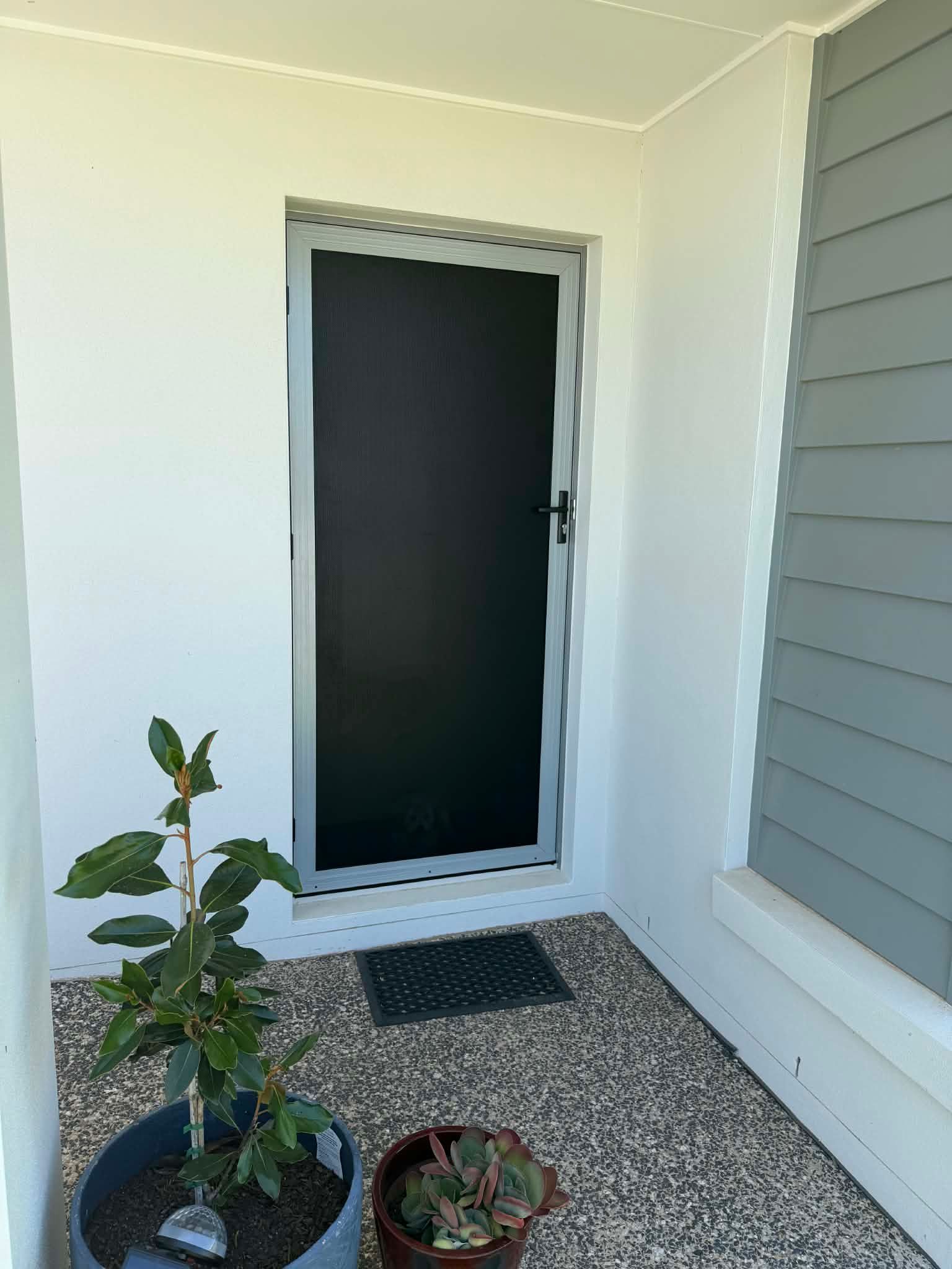 Front porch with a black door, gray siding, and two potted plants on gravel. — Advantage Screens and Blinds Hervey Bay In Pialba, Queensland