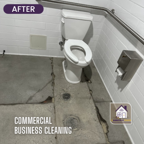 A clean commercial restroom with a toilet, grab bar, and paper towel dispenser. Concrete floor.
