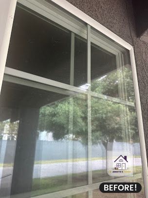 Exterior window with white frame, before cleaning. Reflects trees and a grey building.