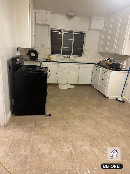 Kitchen with white cabinets, black stove, tan floor, and a window.