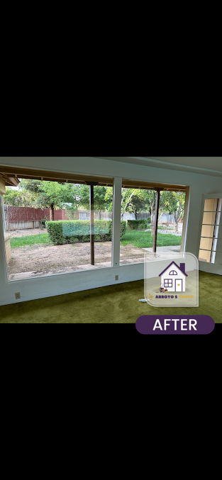 Interior of a room with large windows overlooking a backyard. Green carpet and white walls with