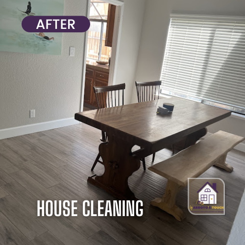Clean dining room with wooden table, bench, and chairs, with a window and a glimpse of the kitchen.
