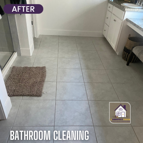 Clean bathroom floor with grey tile, white cabinets, and rug.