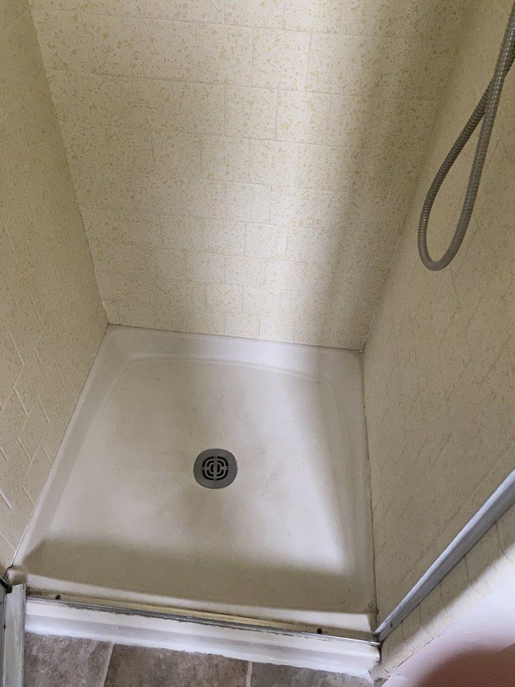 Shower stall with a white base and a drain. Beige walls and a handheld showerhead are visible.