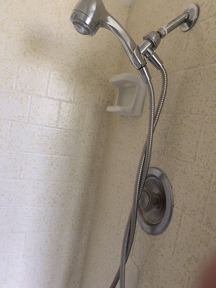 Showerhead with flexible hose and soap dish on a tiled wall.