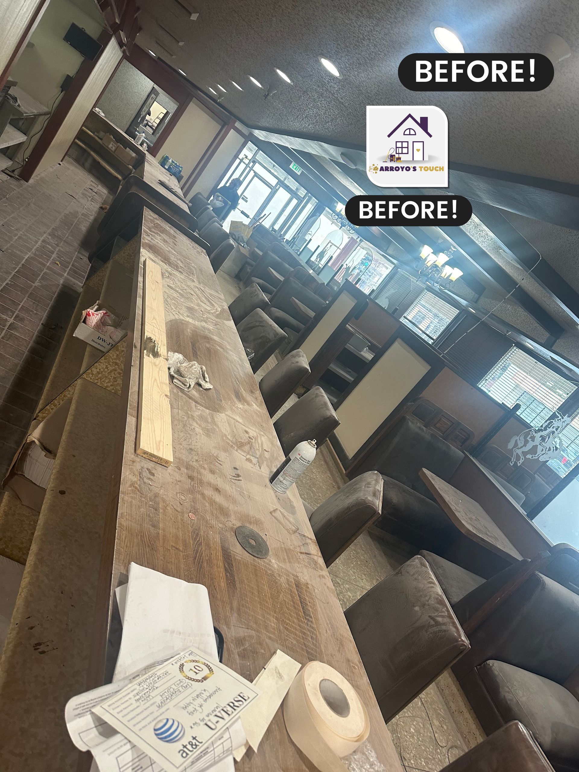 A long, dirty wooden table with attached chairs in a room. 