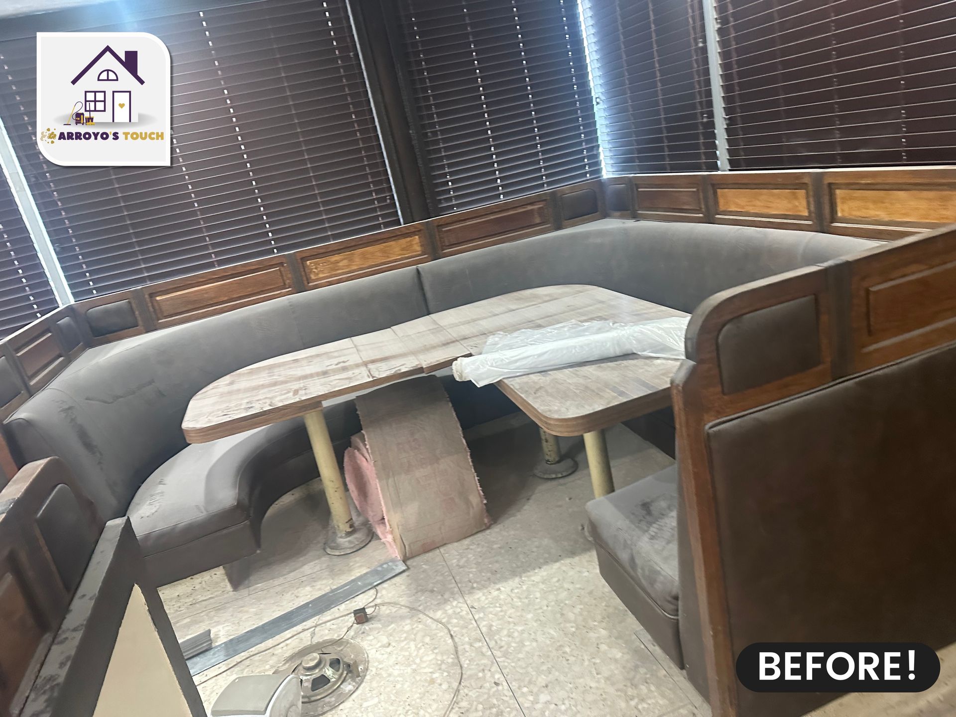 A dirty, worn booth and table in a room with blinds, labeled 