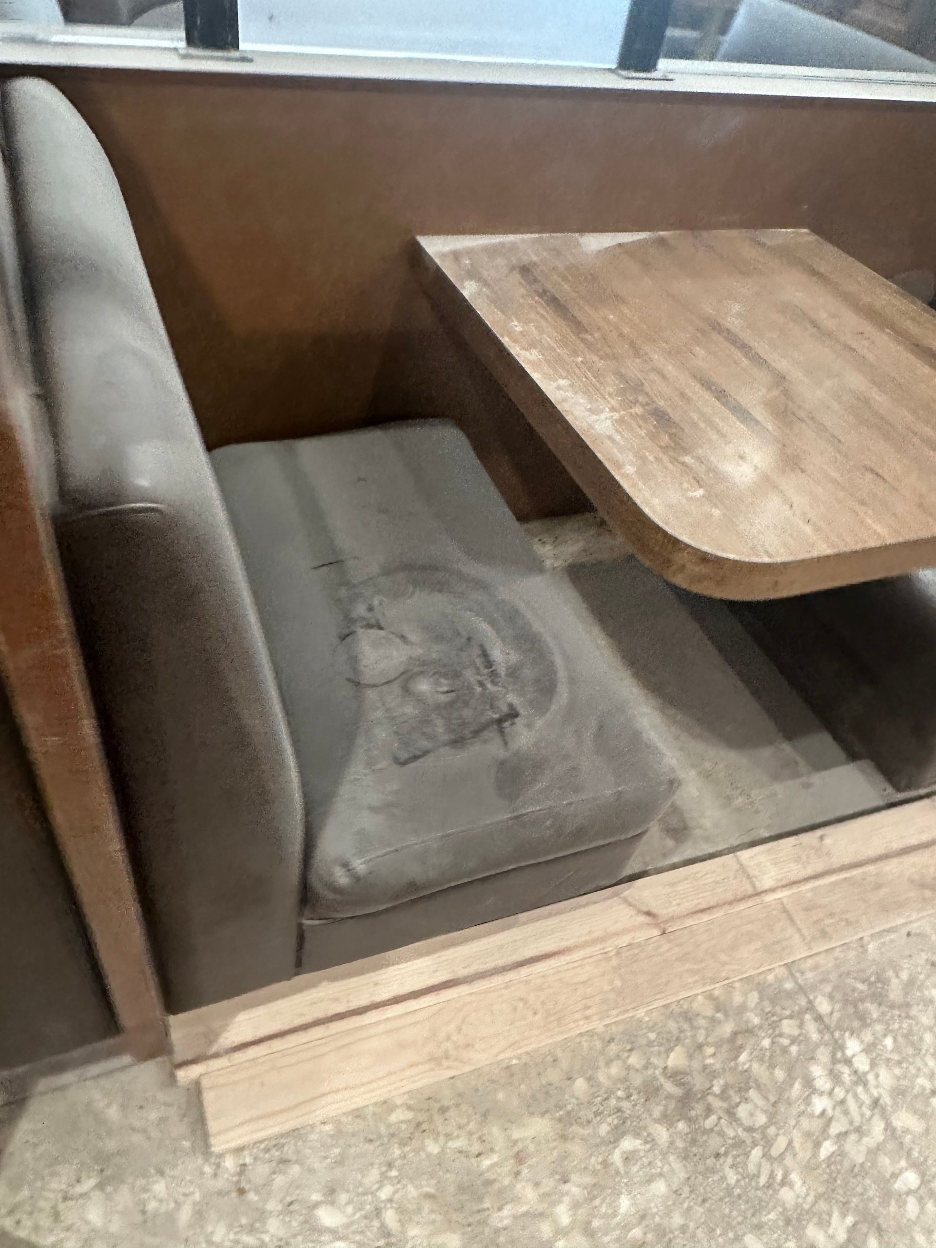 Booth seating with worn, gray upholstery and a wooden table.