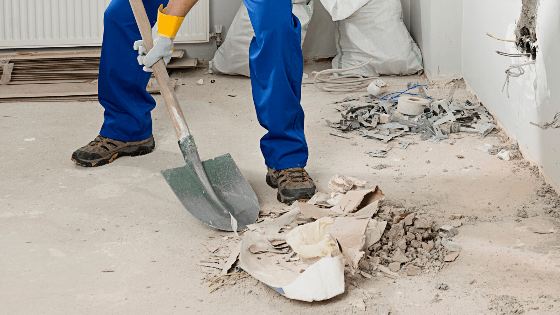 Person in blue overalls shoveling debris from a construction site floor.